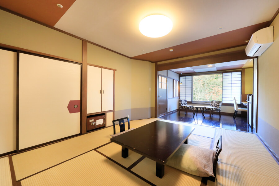 和室と洋室が隣り合ったお部屋。和室部分にはローテーブルと座椅子、金庫などがあり、洋室部分には椅子やテーブルが設置されている。